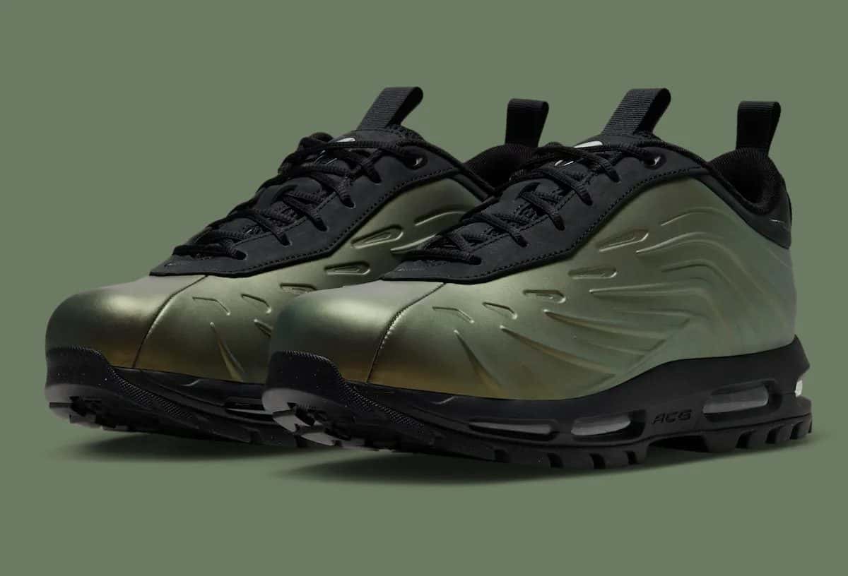 Par de Nike Air Max Goadome Low Foamposite Metallic Gold con carcasa dorada y verdosa, ondas en relieve, cordones negros y suela negra de tacos, sobre fondo verde