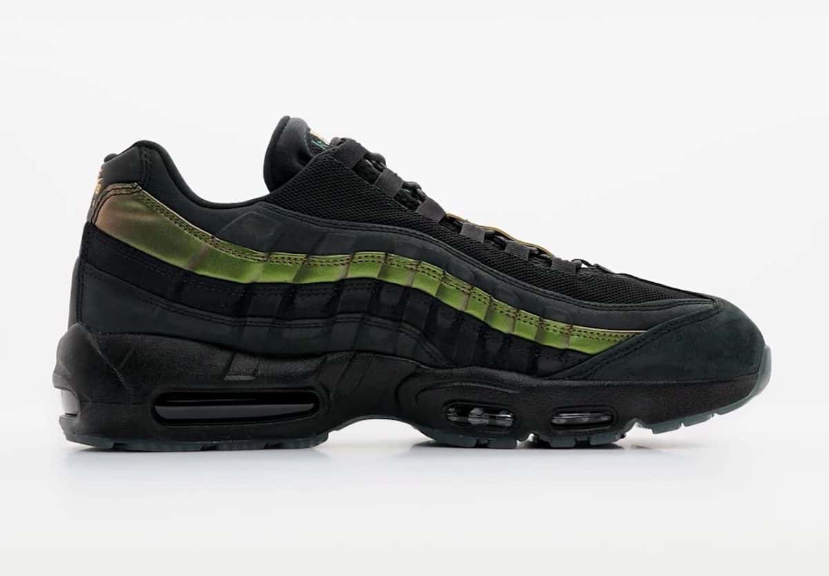 Kyle Wilson x Nike SB Air Max 95 negro de perfil sobre fondo gris claro, con malla y gamuza negras, una franja verde metalizada en los paneles laterales que se vuelve dorada hacia el talón y suela negra