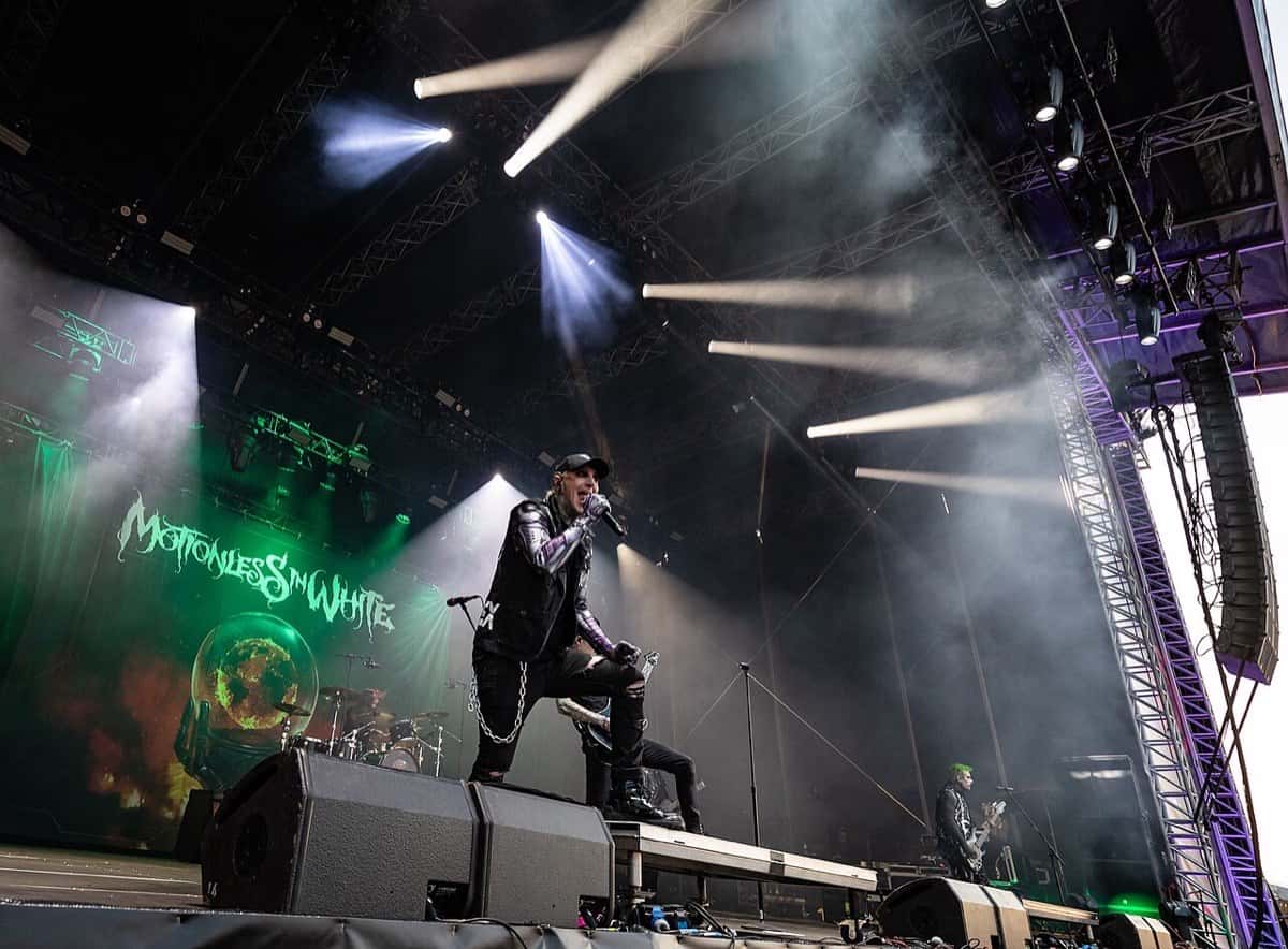 Chris Motionless, cantante de Motionless In White, canta con gorra y campera negra sobre un escenario con luces y humo en el festival Rock am Ring de 2023, con el logo de la banda en la pantalla (foto de archivo)