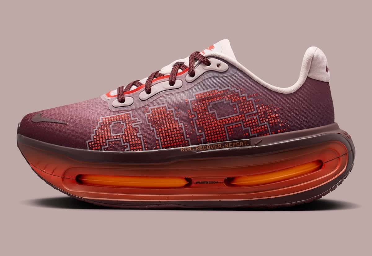 Nike Vomero Premium Shanghai de perfil sobre fondo rosado, con capellada bordó, letras AIR pixeladas en rojo y la unidad Air naranja a la vista en la suela